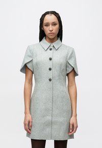 Kortärmad klänning med fiskbensmönster i ljusgrått, med krage och fem svarta knappar framtill. Elegant design.