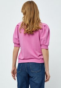 Rosa bomullskofta med korta puffärmar och ribbad mudd, parat med mörkt blå denimjeans. Slät textur med en avslappnad passform.