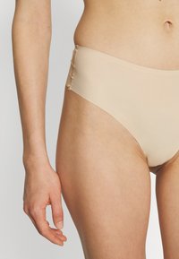 Beige seamless bikini underwear with a high-cut design. Smooth texture and elastic waist with subtle stitching detail on the sides.