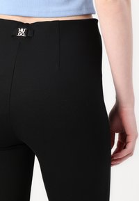 Black leggings made from stretchy material, featuring a smooth texture, high waistband, and a small branded emblem on the back.