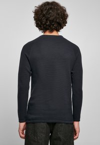 Tamsiai mėlynas ilgas rankovės tekstūruotas marškiniai su raukinėta kaklo ir rankovių apdaila, pasižymintis paprastu dizainu ir tiesiu siluetu, derinamas su tamsiomis kelnėmis.