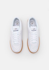 Bílé kožené tenisky s perforovanými detaily, plochými tkaničkami a gumovou podrážkou. Logo Nike na jazyku a po straně.