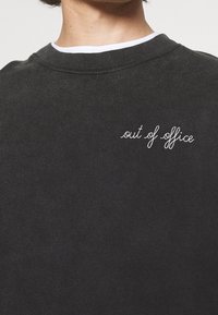 Felpa nera con scollo rotondo; presenta il testo ricamato in bianco "out of office" sul lato sinistro. Texture morbida, design casual.