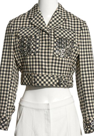 Veste courte à carreaux noir et blanc avec des œillets argentés sur les poches poitrine et les poignets, portée avec un pantalon blanc taille haute.