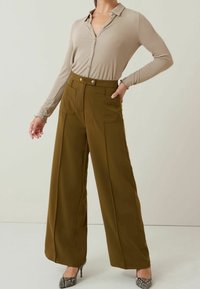 Beige langärmliges Button-up-Shirt, kombiniert mit olivegrünen, weit geschnittenen, taillierten Hosen mit vorderen Taschen und einer glatten Textur.