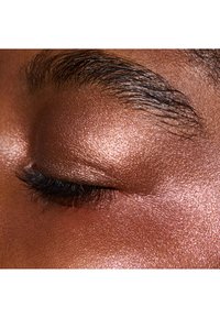 Zbliżenie powieki z błyszczącym różowo-złotym cieniem do powiek, czarnymi rzęsami i gładką, teksturowaną powierzchnią skóry.