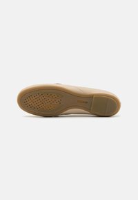 Suela de un zapato en goma beige, con una superficie texturizada que presenta pequeños patrones circulares y surcos laterales para mejorar la tracción.