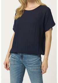 Haut bleu marine à manches courtes en tissu léger avec une coupe décontractée. Encolure arrondie et texture douce, associé à un jean bleu clair.