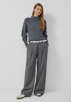 Grijze gebreide coltrui gecombineerd met een grijze gestreepte wijde broek. Een witte riem en sneakers maken de outfit compleet.