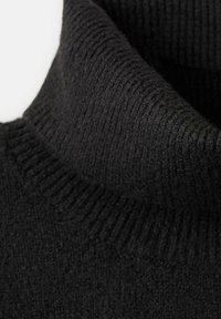 Črn pleten turtleneck pulover s ovratnikom zloženim navzdol, ki prikazuje teksturirano blago in rebrasti detajl v bližnjem posnetku.
