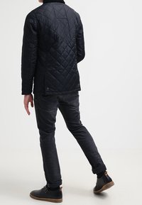 Svart quiltad jacka med hög krage, matchad med mörka jeans och svarta stövlar, som visar en smäcker design och rena linjer.