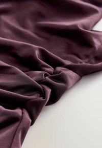 Tissu texturé violet, doux avec une légère brillance, rassemblé en un point, présentant une drapée lisse et des motifs subtils.