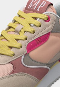 Κοντινό πλάνο πολύχρωμου αθλητικού παπουτσιού με κίτρινα κορδόνια, ροζ και μπεζ πάνελ, και λογότυπο "GAP" στη γλώσσα και την πλαϊνή πλευρά.