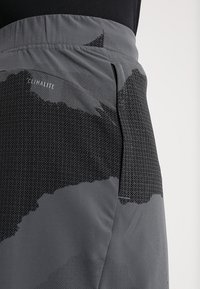 Šedé sportovní šortky s texturovaným, tečkovaným vzorem a hladkým pasem. Štítek „CLIMALITE“ je umístěn blízko horní části.