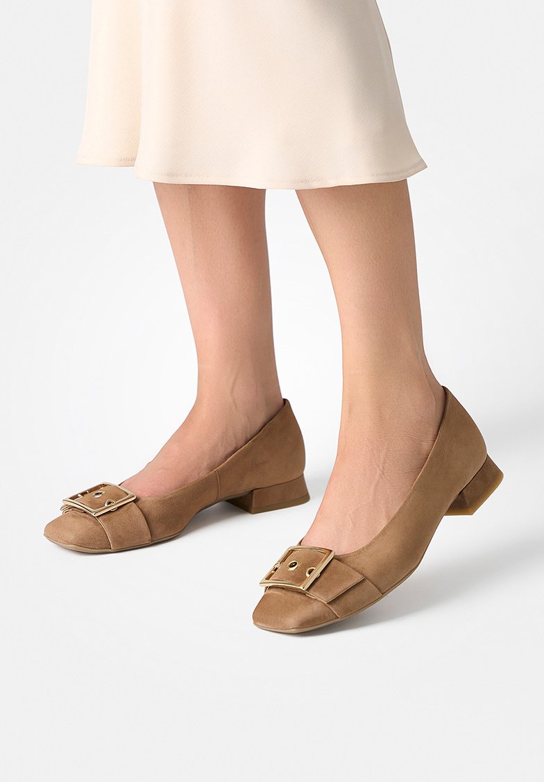 Chaussures à talons bas en daim marron avec un accent carré et un détail de boucle, présentant un bout arrondi et une semelle plate. Texture lisse sur toute la surface.