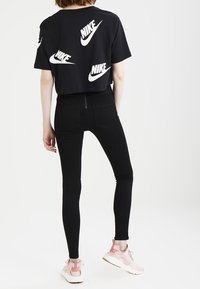 Svart kortärmad t-shirt med vita Nike-logotyper, kombinerad med svarta smala jeans och ljusrosa sneakers. Slen tyg, avslappnad passform.