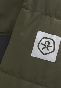 Fjädrande olivgrön tyg med en mjuk textur har en vit logotyp i fyrkantig form, inklusive en stiliserad människogestalt och sköldkontur.