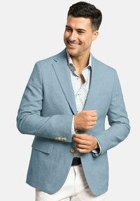 Blazer de lino azul claro con solapas de muesca, dos bolsillos frontales y botones beige, llevado sobre una camisa blanca con pequeños patrones florales.