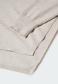 Pull en tricot beige montrant un tissu texturé, des poignets côtelés et un ourlet arrière légèrement plus long. Design minimaliste avec des variations de couleur subtiles.
