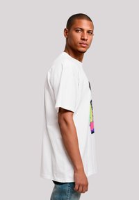 White cotton T-shirt featuring a colorful graphic design with pink and green accents. The shirt has a relaxed fit and short sleeves.