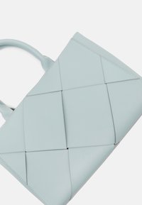 Lyseblå læderhandtaske med et vævet design, struktureret form, runde håndtag og synlige syninger.