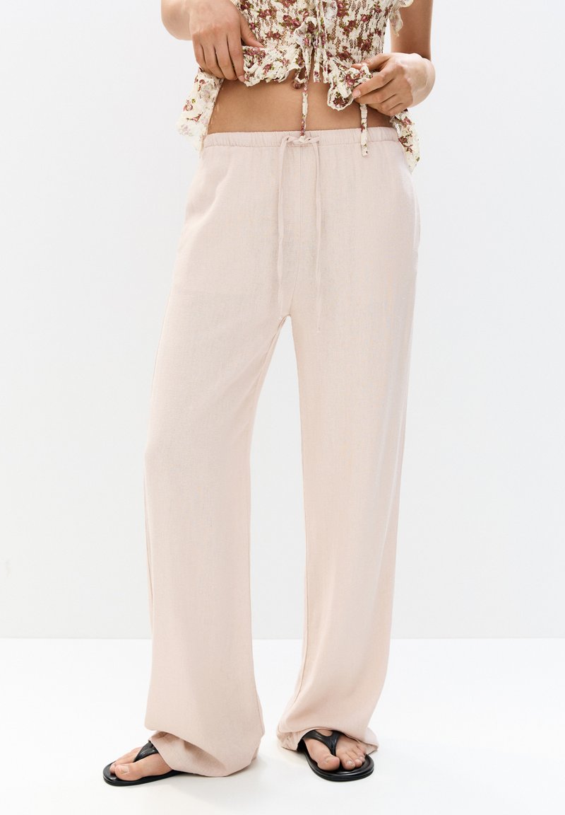 Helle pinke weit geschnittene Hose aus einem weichen, glatten Material mit einem Kordelzugbund. Sie zeichnet sich durch eine gleichmäßige Textur und minimale Nähte aus.