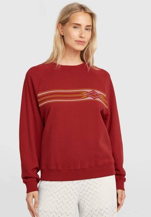 Rdeča jopa z dolgimi rokavi in okroglim izrezom; na prsih ima vodoravne proge v oranžni in roza barvi. Mehka tekstura tkanine, sproščen kroj.