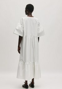 Witte katoenen jurk met korte pofmouwen, gelaagde ruchezoom en een relaxed fit. Soepele textuur en enkel-lange ontwerp.