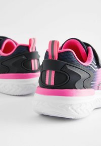 Baskets de sport avec une tige en mesh noir, des accents roses et une semelle blanche ; dotées d'un talon texturé et d'une poignée rayée.