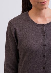 Tmavě hnědý cardigan vyrobený z měkkého materiálu, s kulatým výstřihem a pěti knoflíkovými zapínáními vpředu. Úzké žebrované manžety.