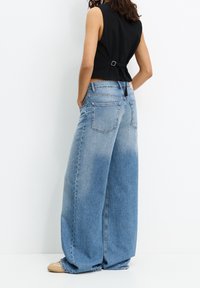 Jeans en denim bleu à jambes larges avec un délavage léger, dotés de poches arrière et d'une taille mi-haute, associés à un haut sans manches noir.