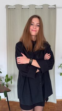 Camisa negra extragrande con botones y mangas largas, usada sobre un vestido negro. La modelo tiene el cabello largo y castaño claro y los brazos cruzados.