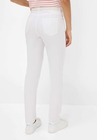 Witte, slim-fit broek met twee achterzakken, riemlussen en een gladde textuur. Draagt in combinatie met witte sneakers, minimale details.