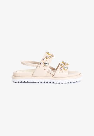 Sandalias beige con dos correas anchas, adornadas con piedras preciosas claras y en tonos pastel, y una suela blanca y dentada para mayor tracción.