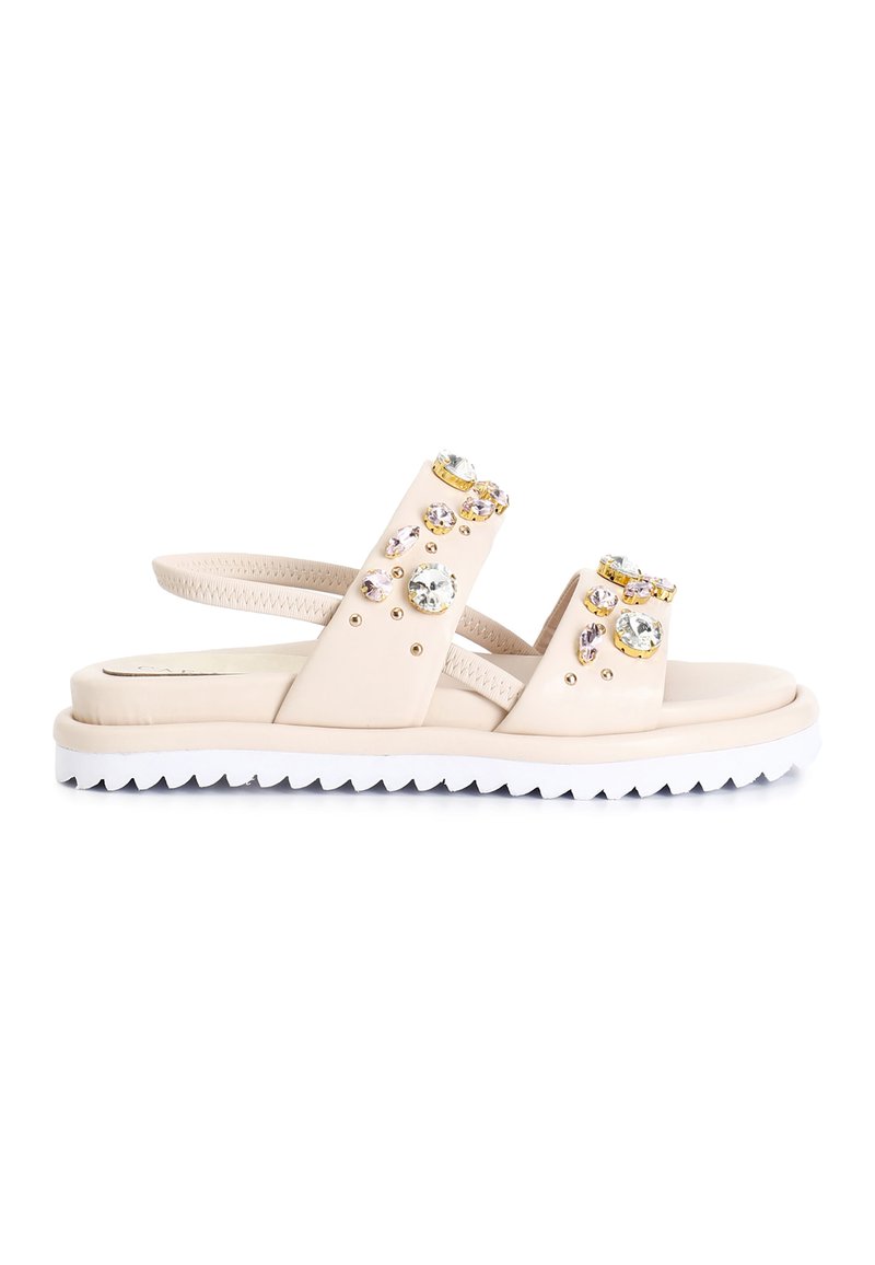 Beige sandals with two wide straps, adorned with clear and pastel gemstones, and a white, jagged sole for traction.