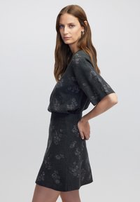 Donkergrijze twee-delige outfit bestaande uit een top met korte mouwen en een uitlopende rok met subtiele bloemenpatronen. De stof heeft een zachte textuur.