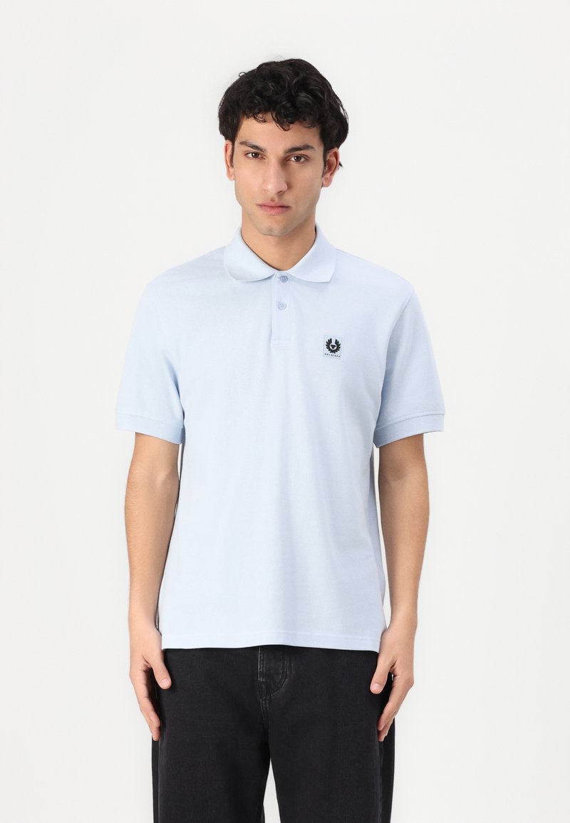 Ανοιχτό μπλε πόλο μπλουζάκι από βαμβάκι, με κλασικό γιακά, κοντά μανικιά και μία μικρή μαύρη ετικέτα λογότυπου στο αριστερό στήθος.