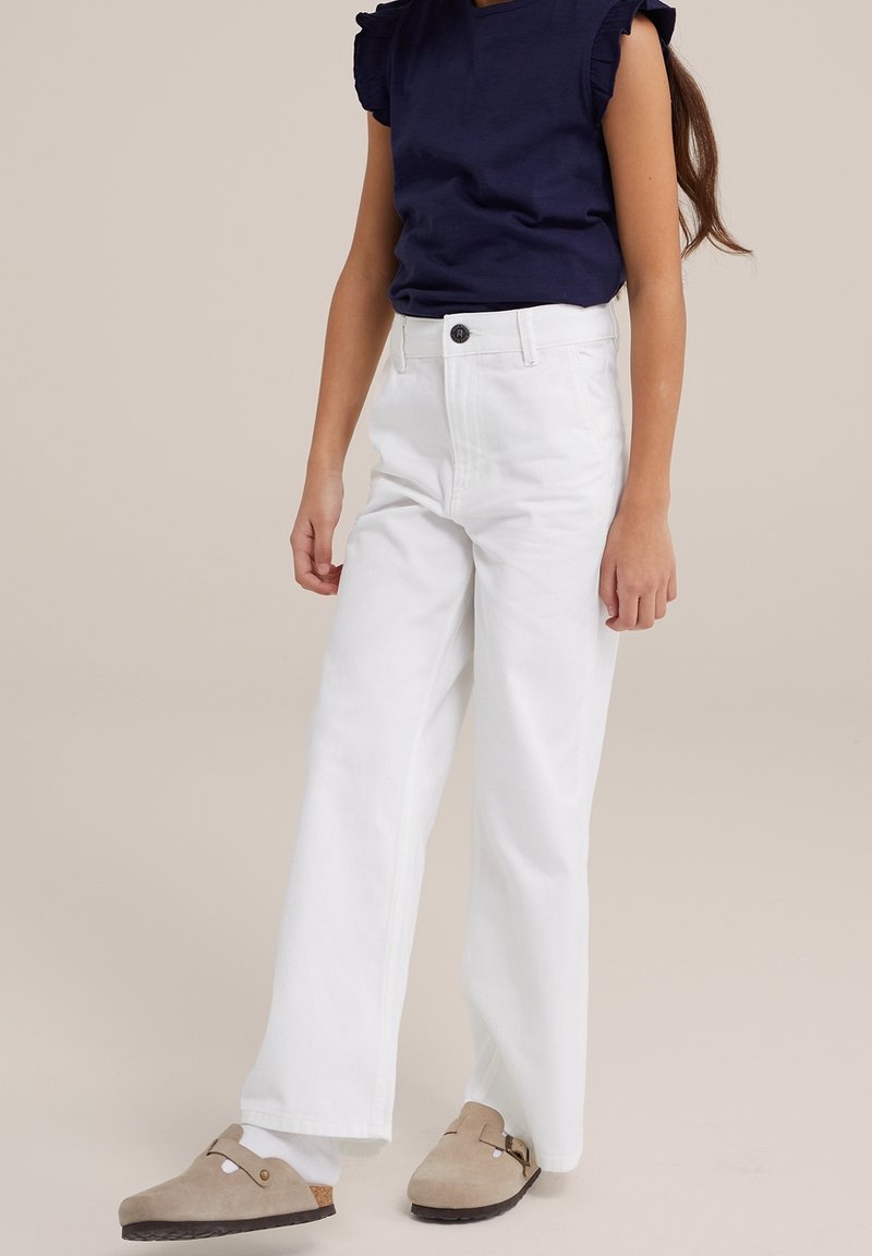 Witte wijde jeans met een hoge taille, voorzien van een sluiting met een knoop aan de voorkant en zijzakken. Gepaard met een marineblauw shirt met korte mouwen en beige schoenen.