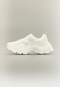 Λευκό αθλητικό παπούτσι με υφασμάτινο επάνω μέρος με υφή και λείες δερμάτινες λεπτομέρειες, με στρογγυλεμένη μύτη, παχιά σόλα και αντίθετη ραφή.