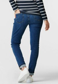 Mörkblå jeans i slim fit med uppvikta fållar, två bakfickor och en mjuk textur, tillsammans med vita sneakers.