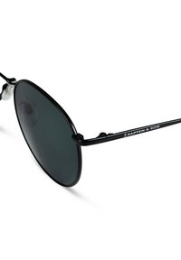Occhiali da sole in stile black metal con lenti grigio scuro. Presentano un design leggero e un logo inciso sulla stanghetta. Montatura curva e bracci sottili.