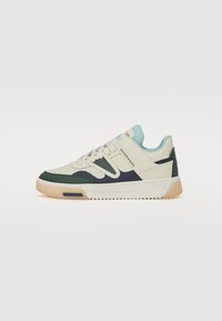 Sneakers featuring a cream upper, green and navy accents, smooth and textured panels, lace closure, and a gum rubber sole.