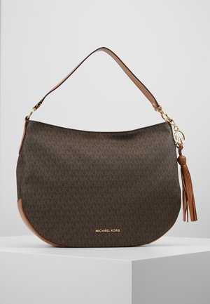 Brązowa torba na ramię Michael Kors z monogramem, rączka ze skóry w kolorze jasnobrązowym, złota zawieszka z logo i detal z frędzlem, prezentowana na białym stojaku.