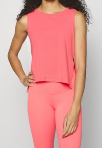 Top sin mangas rosa con un corte relajado, combinado con leggings rosa a juego. La tela parece suave con una textura lisa.