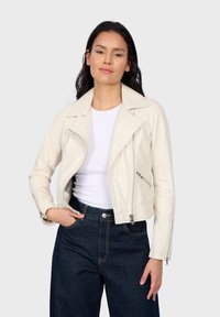 Witte leren cropped jack met zilveren ritsen, gekartelde kraag en zijzakken, gecombineerd met donkere spijkerbroek en een witte top.