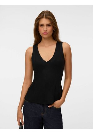 Jeune femme aux longs cheveux bruns portant un haut noir sans manches à col en V et un jean foncé, avec une main dans la poche et tenant un sac à main noir.
