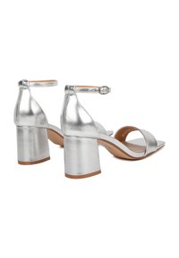 Sandali alti metallici argento con punta quadrata, due cinturini e cinturino alla caviglia. Tacco a blocco spesso per stabilità. Texture liscia.