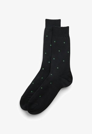 Schwarze Socken mit einer glatten Textur, die grüne, sternförmige Muster gleichmäßig über den Stoff verteilt und einen gerippten Bund aufweisen.
