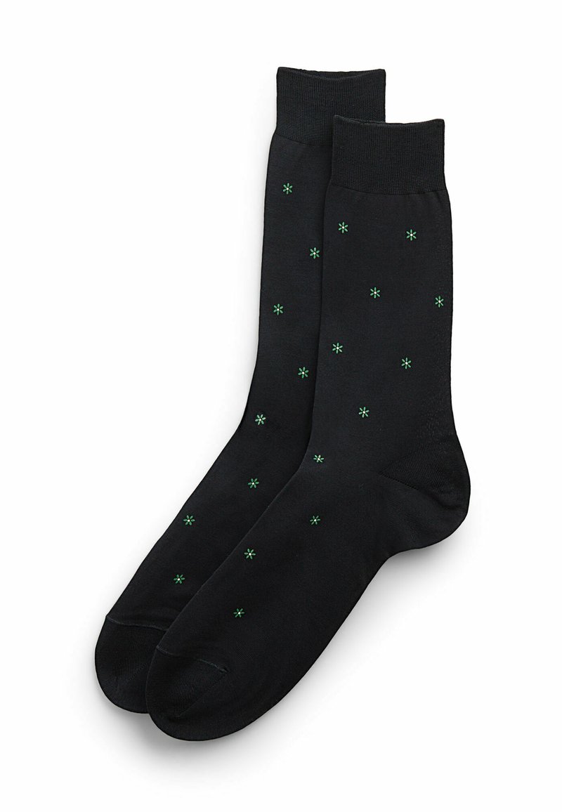 Czarne skarpetki o gładkiej fakturze, z zielonymi wzorami w kształcie gwiazdek równomiernie rozmieszczonymi w całym materiale oraz prążkowanym ściągaczem.