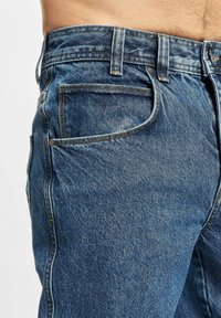 Denim-Jeans in einer mittelblauen Waschung mit einer verblassten Textur, Fünf-Taschen-Design und sichtbaren Nähten entlang der Nähte.
